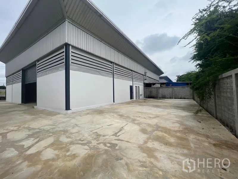 Warehouse for rent or sale in Sai Noi, Nonthaburi - Warehouse exterior with louvered vents, metal roof and expansive concrete yard.