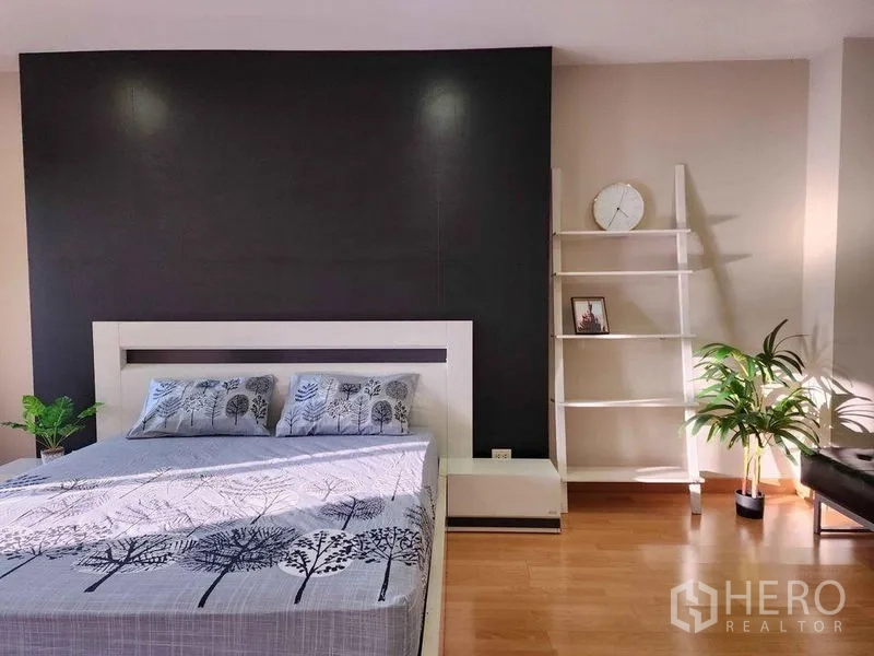 Condominium for rent in Khlong Toei, Bangkok - Bright bedroom with black accent wall, white bed, ladder shelf and indoor plants on wood flooring.