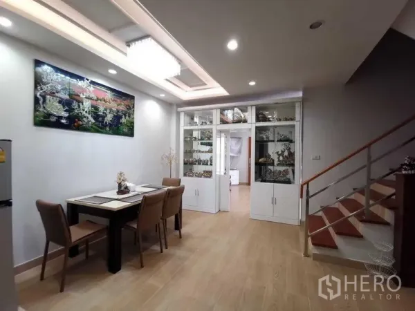 Detached House for rent in Prawet, Bangkok - Dining area with four‑seat table, recessed ceiling lights, built‑in glass cabinets and staircase.