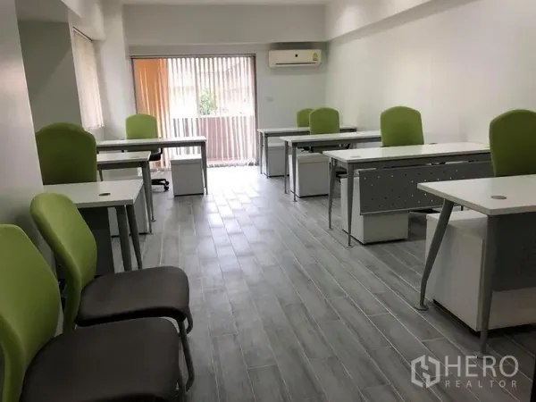 Office Space for rent in Khlong Toei, Bangkok - Long office room with multiple workstations facing a balcony with vertical blinds and abundant natural light.