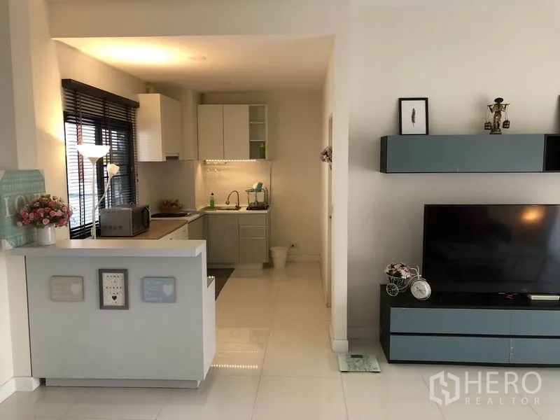 Townhouse for rent in Saphan Sung, Bangkok - Open-plan living with compact kitchen, glossy cabinets, TV wall and dark window blinds