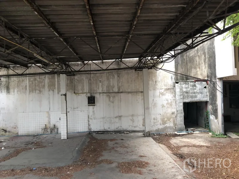 Home Office for rent in Khlong Toei, Bangkok - Shaded carport with metal roof and weathered concrete wall, suitable for parking or loading.