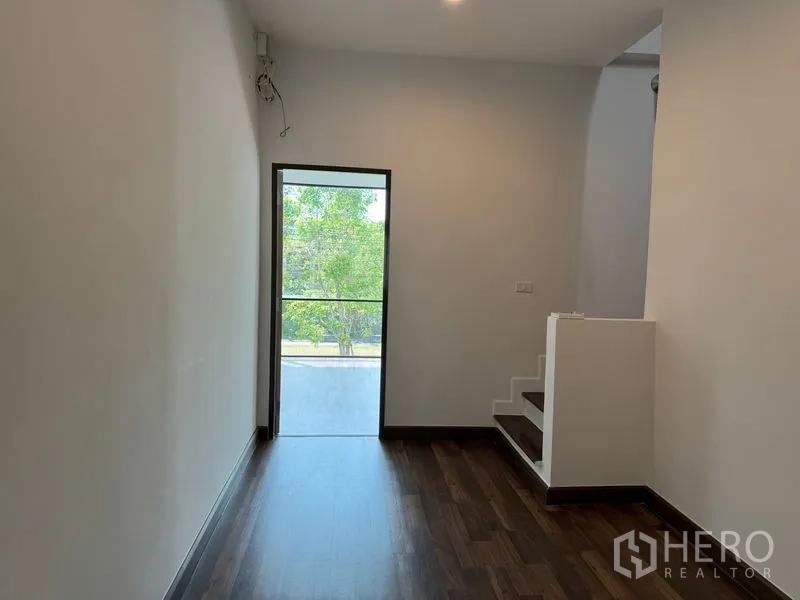 สำนักงานที่บ้าน ให้เช่าหรือขายในBang Na, Bangkok - โถงชั้นบน พื้นไม้เข้ม พร้อมประตูกระจกออกสู่ระเบียงวิวต้นไม้