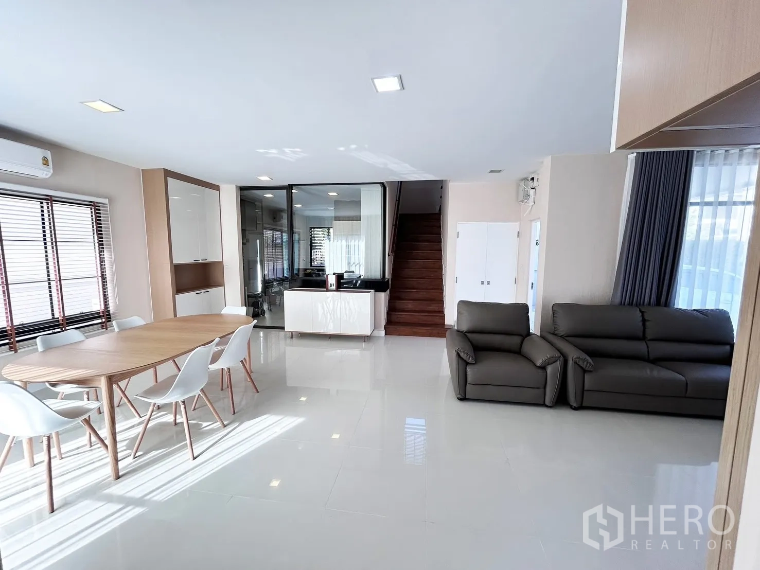 Detached House for rent or sale in Prawet, Bangkok - Open-plan living and dining area with large floor tiles, dining set, sofas and a staircase.