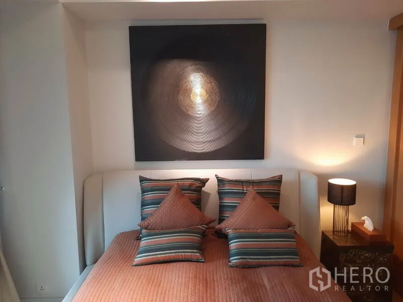 Condominium for rent or sale in Sathon, Bangkok - Cozy bedroom with upholstered headboard, striped pillows and a bedside lamp.