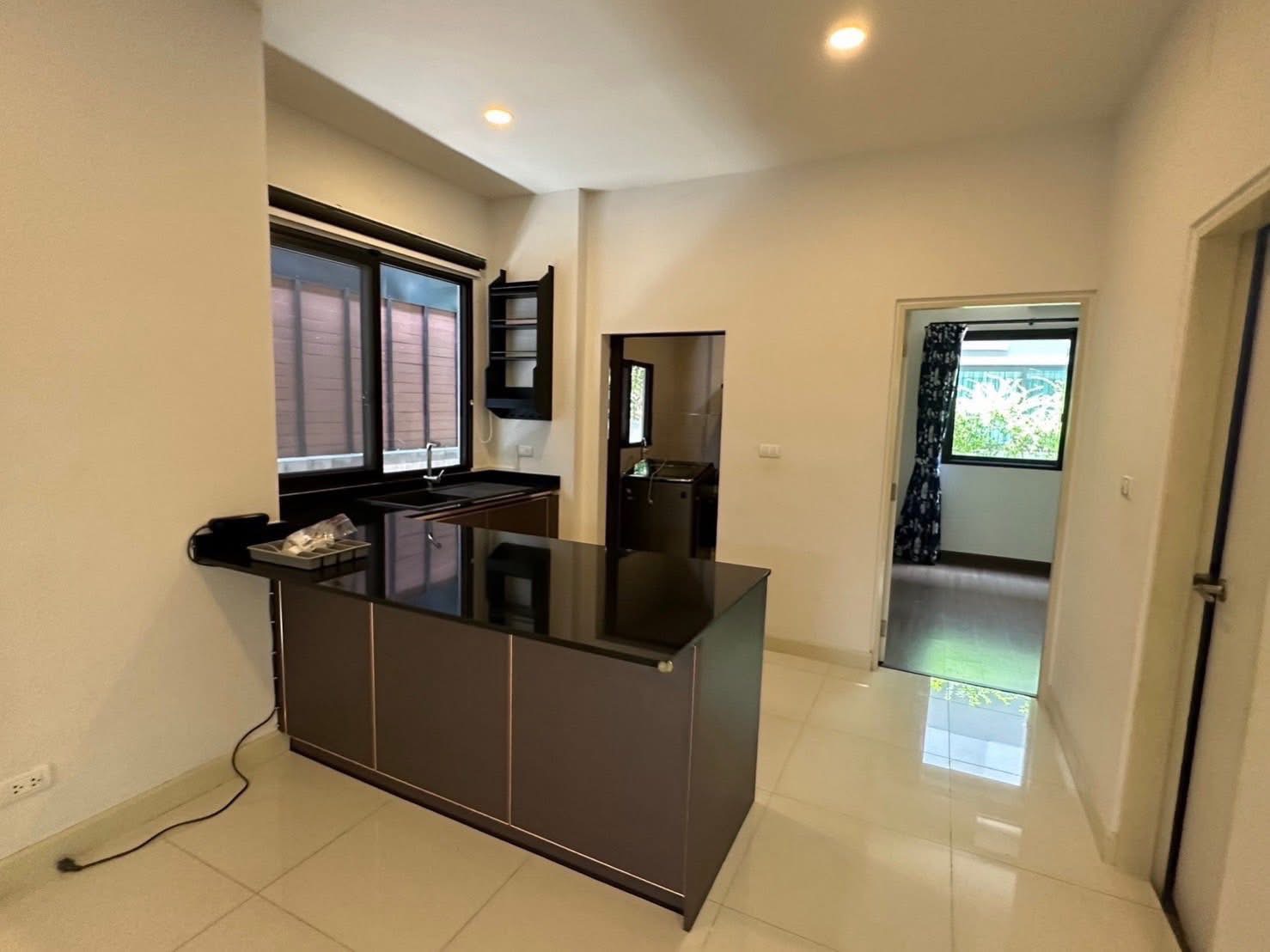 Detached House for rent in Bang Phli, Samut Prakan - Pantry kitchen with black stone countertop, large windows and doorway leading to a bedroom.