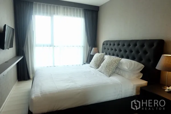 คอนโด ให้เช่าในKhlong Toei, Bangkok - ห้องนอนหลักหัวเตียงบุหนังแบบปุ่ม หมอนอิง โทรทัศน์ติดผนัง และหน้าต่างบานใหญ่ที่ไลฟ์ คอนโดมิเนียม