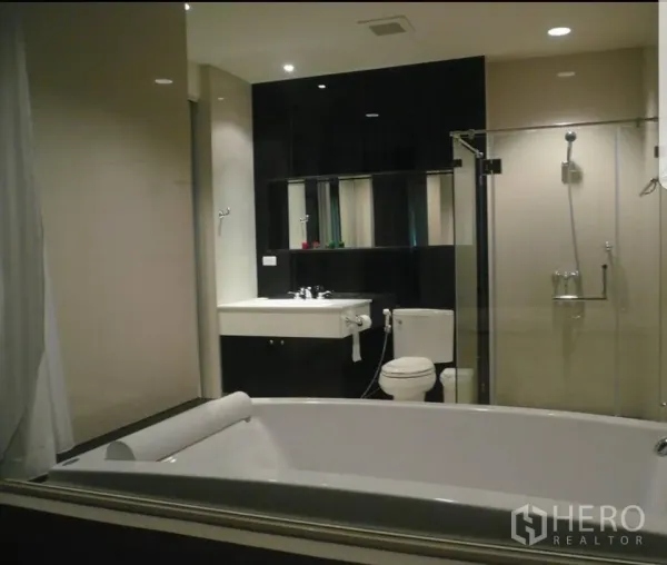 公寓 出租在Pathum Wan, Bangkok - 现代卫浴，带大浴缸、玻璃淋浴间、坐便与台盆，嵌灯照明。