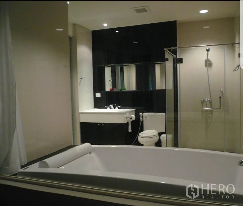 公寓 出租在Pathum Wan, Bangkok - 现代卫浴，带大浴缸、玻璃淋浴间、坐便与台盆，嵌灯照明。