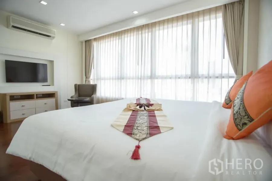 Apartment for rent in Khlong Toei, Bangkok - Sunlit bedroom with large windows, wall-mounted TV and air conditioning in a modern Bangkok apartment.