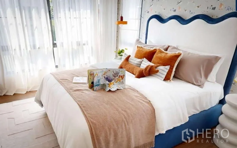 Detached House for rent in Bang Phli, Samut Prakan - Children’s bedroom with blue upholstered headboard, playful wallpaper and soft cushions beside sheer curtains.