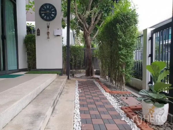 บ้าน ให้เช่าในBang Kapi, Bangkok - สวนข้างบ้านพร้อมทางเดินแผ่นทางเท้า โรยหินสีขาว ต้นไม้ใหญ่และแนวพุ่มไม้ ข้างประตูกระจก.