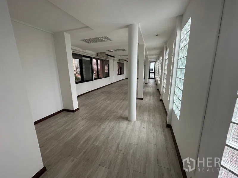 Office Space for rent in Sathon, Bangkok - Corridor view of open office with round columns, glass-block windows and views to neighboring buildings.