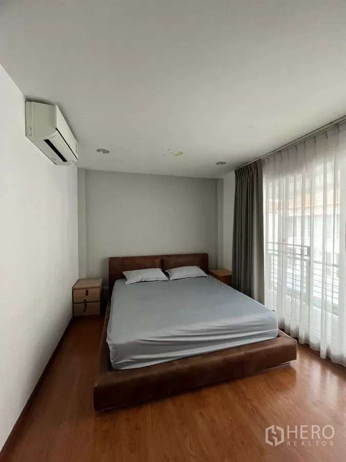 Townhouse for rent in Chom Thong, Bangkok - Bright master bedroom with large bed, wood flooring and sheer curtains.