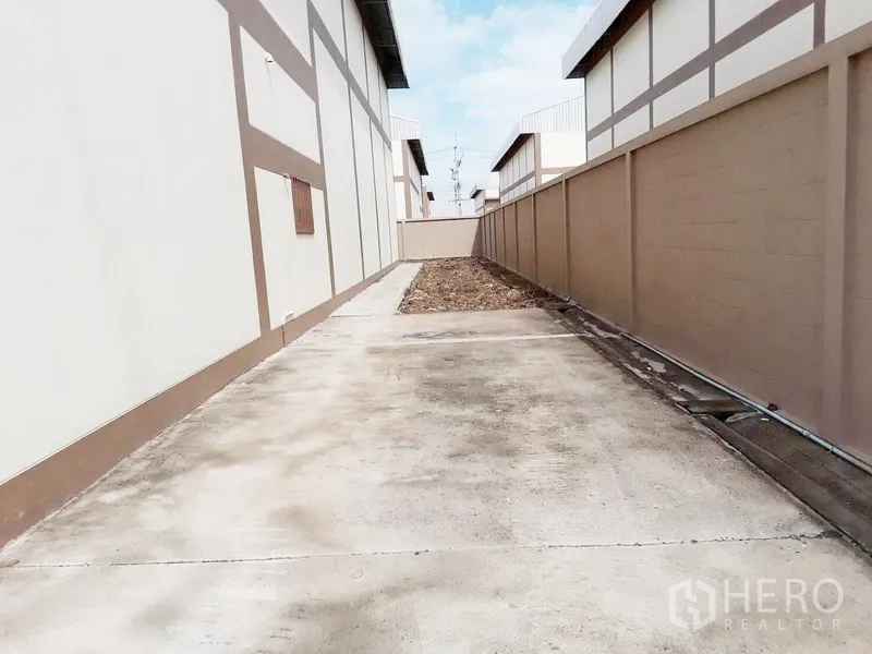 工厂 出租或出售在Pathum Thani - 厂房之间的混凝土侧通道，旁有高墙围护。