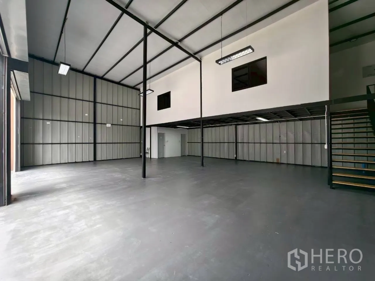 Warehouse for rent in Suan Luang, Bangkok - Angled shot of high-clearance warehouse with black steel structure, stairs to mezzanine, and epoxy floor.