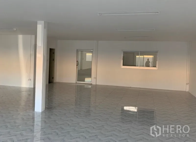 Warehouse for rent in Samut Prakan - Large tiled office area inside the warehouse with white walls, window and sliding glass door.