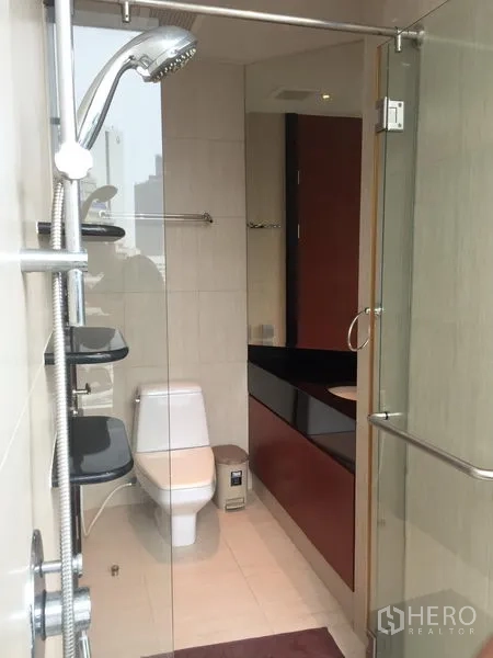 Condominium for rent or sale in Bang Rak, Bangkok - Guest bathroom with glass shower enclosure, toilet, and long vanity.