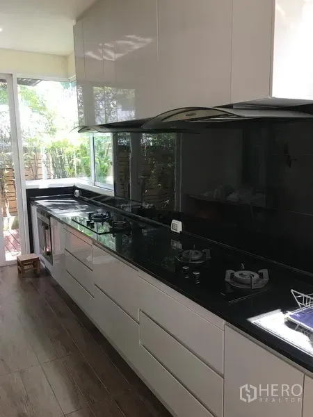 ทาวน์เฮาส์ ขายในHuai Khwang, Bangkok - ครัวสไตล์โมเดิร์นเคาน์เตอร์หินแกรนิตสีดำ เตาแก๊ส และหน้าต่างมองสวน