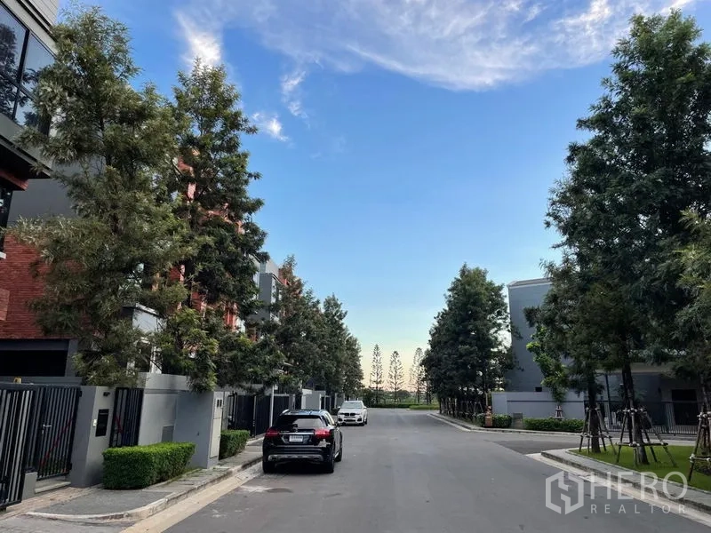 联排别墅 出售在Lat Phrao, Bangkok - 社区内林荫道路，门前可见联排别墅与车辆。