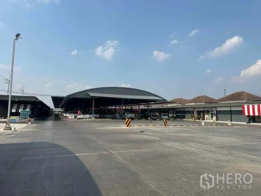 พื้นที่ขายปลีก ให้เช่าในPathum Thani - ลานคอนกรีตกว้างพร้อมอาคารตลาดหลังคาโค้งและทางเข้าออก ใต้ท้องฟ้าโปร่ง