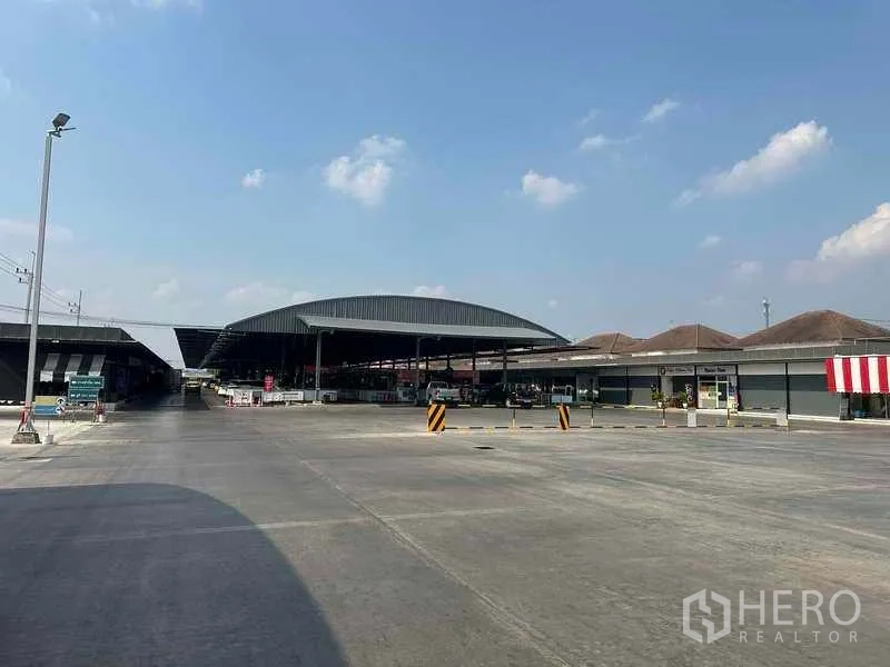 พื้นที่ขายปลีก ให้เช่าในPathum Thani - ลานคอนกรีตกว้างพร้อมอาคารตลาดหลังคาโค้งและทางเข้าออก ใต้ท้องฟ้าโปร่ง