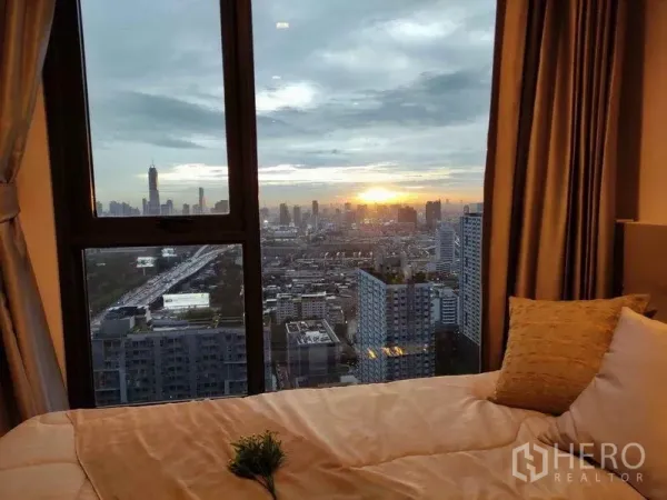 公寓 出租在Ratchathewi, Bangkok - 卧室窗外日落城市景观，前景为床与抱枕。