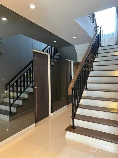 Detached House for sale in Prawet, Bangkok - Hallway with mirrored feature wall and wooden staircase to the upper floor.
