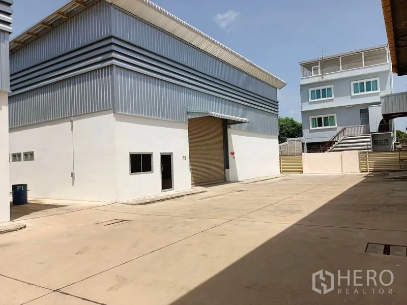 Warehouse for rent in Suan Luang, Bangkok - Modern warehouse exterior with a roller shutter and large paved loading yard.