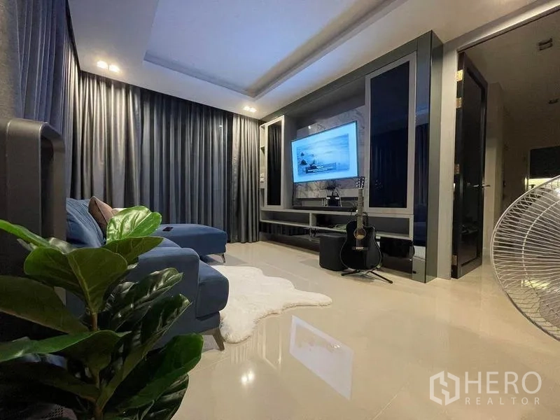 Detached House for rent - Cozy living room with blue sectional sofa, TV wall unit and dark curtains.