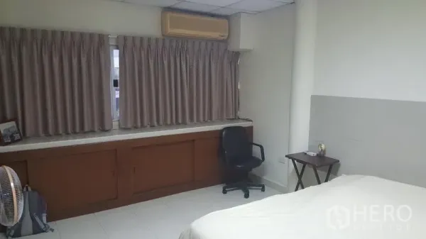 Shophouse for sale in Khlong Toei, Bangkok - Bright bedroom with large curtained windows, built-in cabinet, air conditioner, desk and chair.