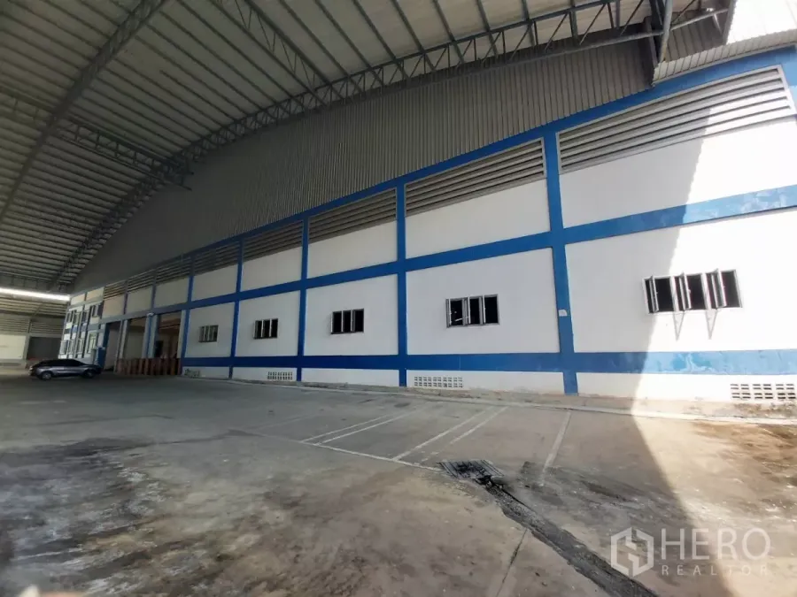 คลังสินค้า ให้เช่าในBang Bo, Samut Prakan - ลานโหลดสินค้าคลุมหลังคาข้างอาคารโกดังโทนขาว–น้ำเงิน หลังคาสูงโปร่ง