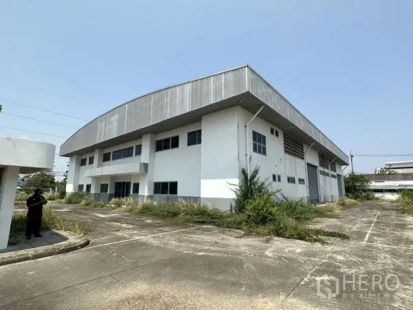 โรงงาน ให้เช่าในChon Buri - ภาพภายนอกด้านข้างของโรงงานสองชั้น ทางวิ่งคอนกรีตกว้างและกันสาดยื่น