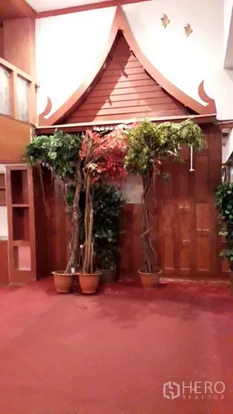 零售空间 出租在Watthana, Bangkok - 泰式屋脊装饰特色墙，摆放室内绿植与红色地毯。