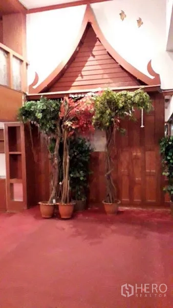 零售空间 出租在Watthana, Bangkok - 泰式屋脊装饰特色墙，摆放室内绿植与红色地毯。