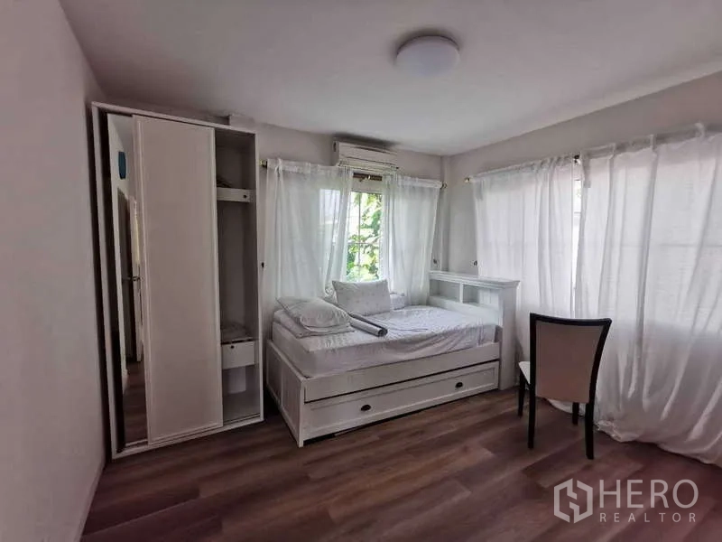 บ้าน ให้เช่า - ห้องนอนสว่าง เตียงเดี่ยวแบบลิ้นชัก ตู้เสื้อผ้า เก้าอี้ และผ้าม่านโปร่งรอบหน้าต่าง