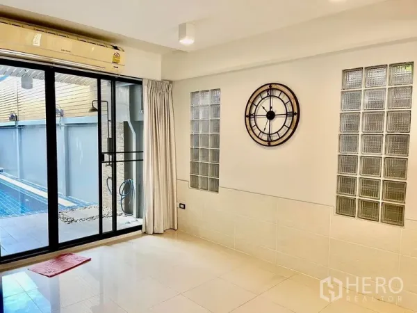 Townhouse for rent in Khlong Toei, Bangkok - Living area with decorative clock and sliding glass doors opening to a private pool.