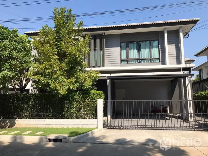 Detached House for rent in Bang Phli, Samut Prakan - Modern two-storey detached house with gated driveway, covered carport and lush hedges.