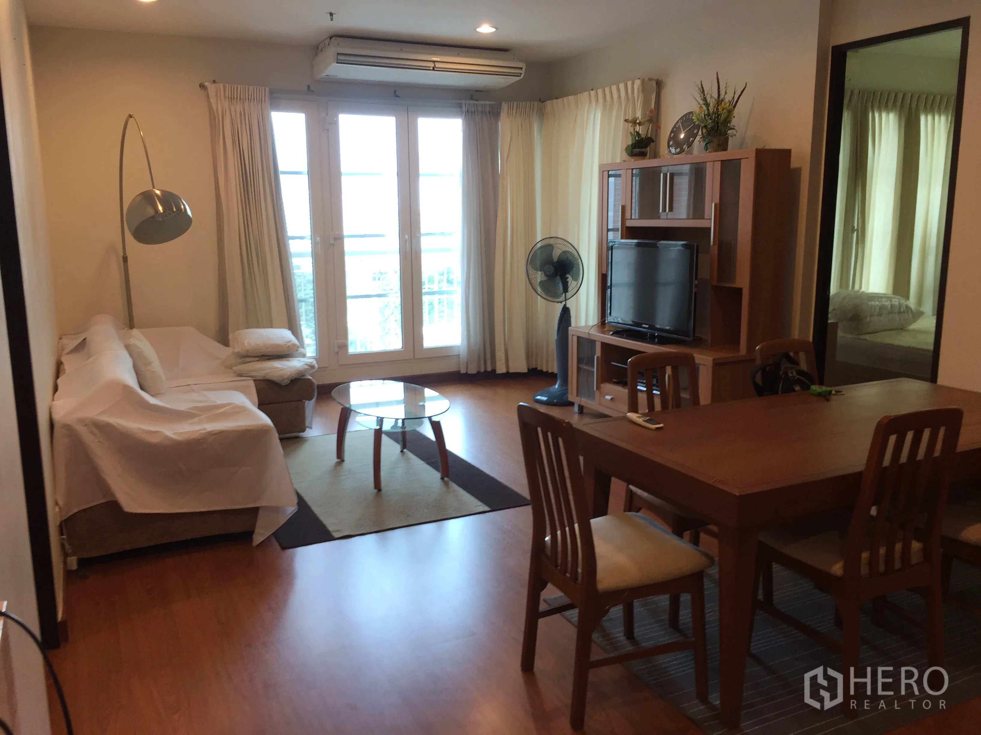 คอนโด ให้เช่าในKhlong Toei, Bangkok - ห้องนั่งเล่นมีโซฟา ชั้นวางทีวี ชุดโต๊ะกินข้าว และประตูระเบียงพร้อมผ้าม่าน