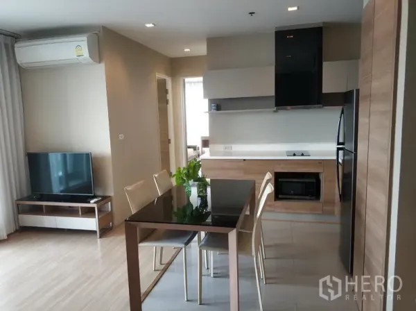 คอนโด ให้เช่าในPhaya Thai, Bangkok - ครัวและโซนทานอาหารแบบเปิด โทนไม้พร้อมโต๊ะกระจกและมุมทีวีในคอนโดสมัยใหม่