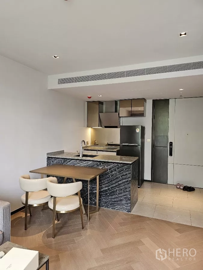 公寓 出租在Watthana, Bangkok - 开放式厨房带石材中岛、双人餐桌与嵌入式家电，靠近入户门。