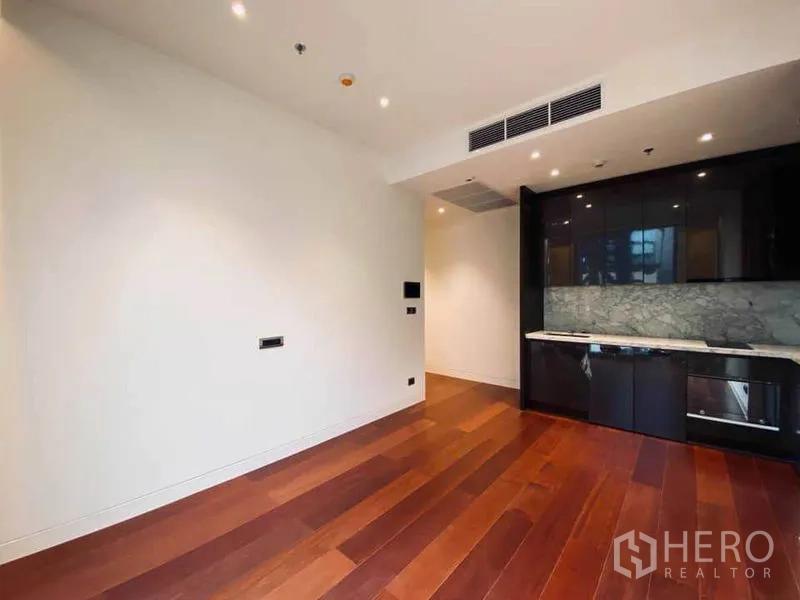 Condominium for sale in Watthana, Bangkok - Open-plan living area with warm wooden floors and a glossy black kitchenette with marble backsplash.