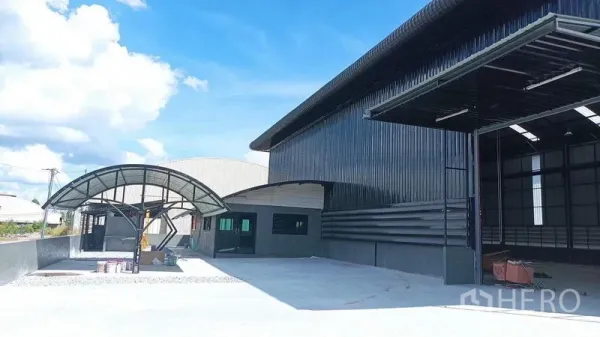 Warehouse for rent in Ban Bueng, Chon Buri - Close view of the warehouse facade with an open loading door, curved canopy, and spacious driveway.