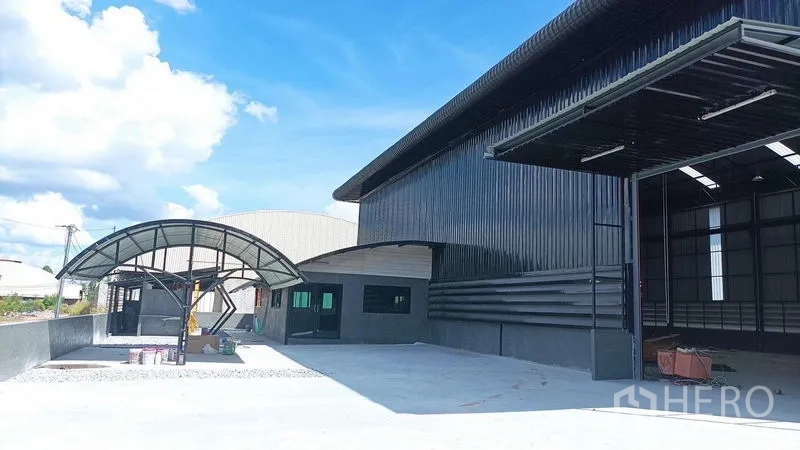 Warehouse for rent in Ban Bueng, Chon Buri - Close view of the warehouse facade with an open loading door, curved canopy, and spacious driveway.