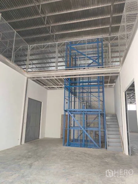 Warehouse for rent in Krathum Baen, Samut Sakhon - Blue caged cargo lift and stairs providing access to the mezzanine inside the warehouse.