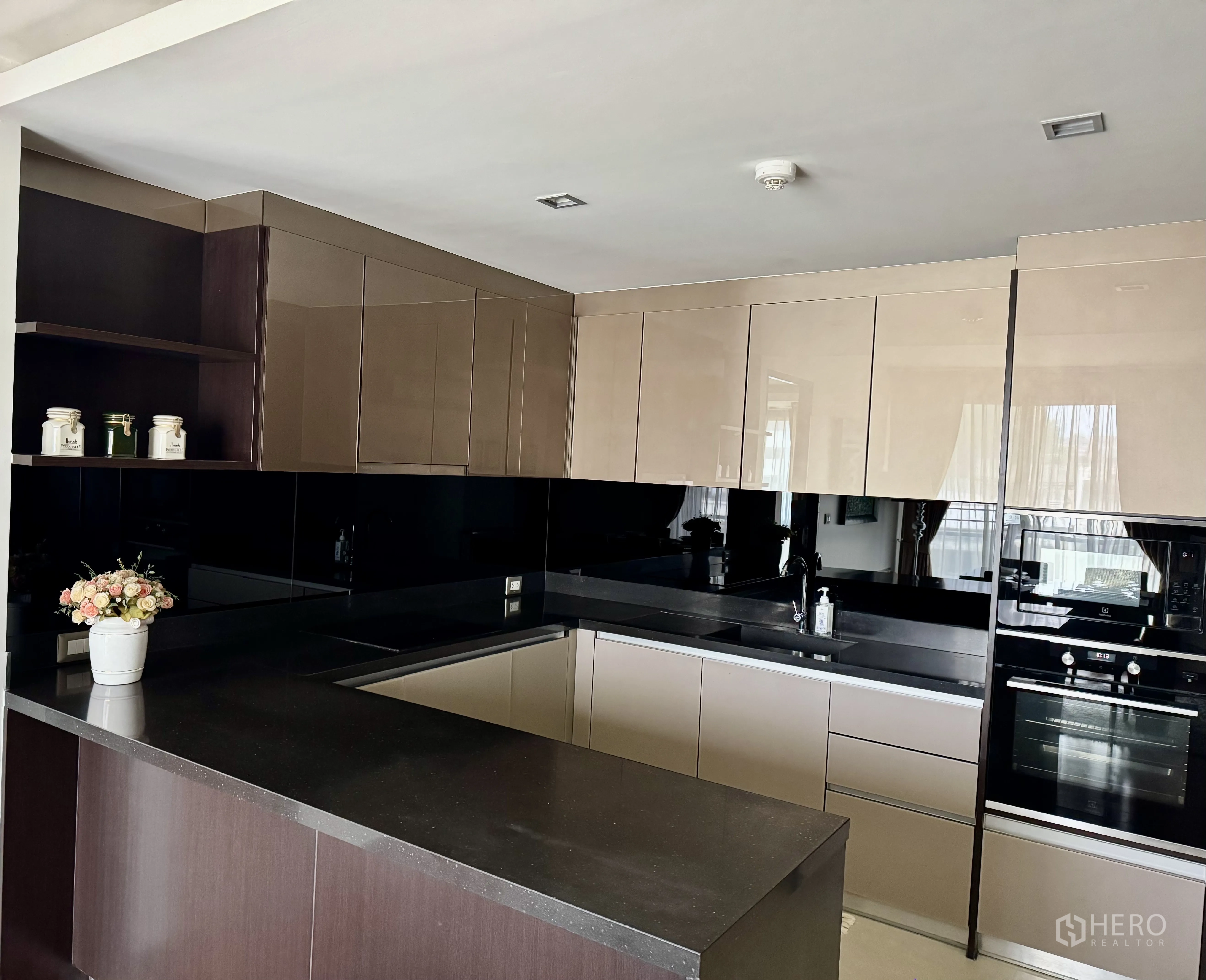 Condominium for rent in Watthana, Bangkok - U-shaped kitchen with black stone countertop, built-in oven, and microwave.