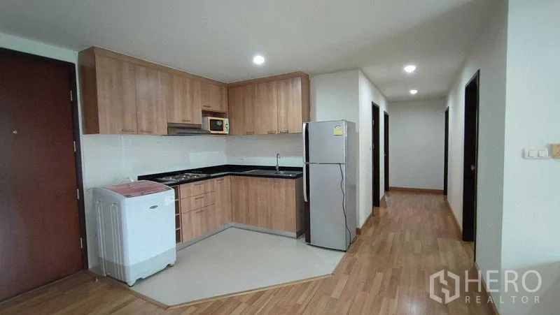 คอนโด ให้เช่าในKhlong Toei, Bangkok - ครัวรูปตัวแอล ตู้ไม้ เคาน์เตอร์หินสีดำ ตู้เย็น เครื่องซักผ้า และโถงทางเดินสู่ห้องนอน