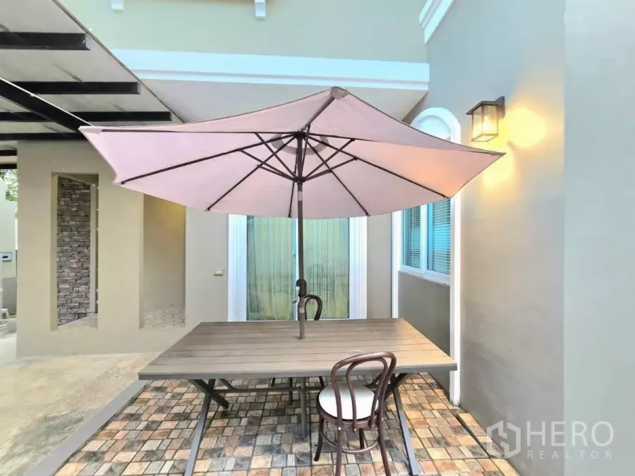 Detached House for rent in Samut Prakan - Cozy patio with a large parasol, wooden table and chairs beside sliding glass doors.
