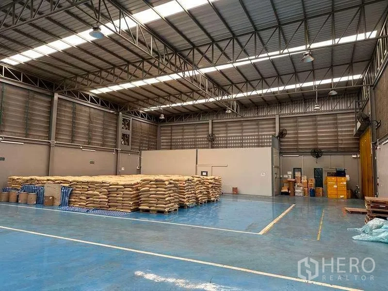 Factory for rent in Samut Prakan - Spacious warehouse floor with high ceiling, skylights and stacked pallets.