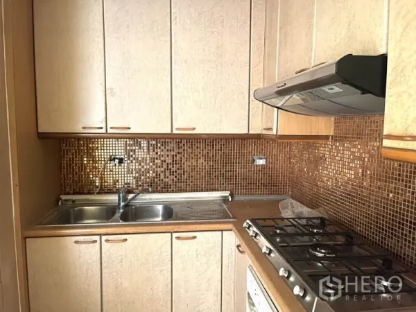 公寓 出租在Watthana, Bangkok - 紧凑厨房，燃气灶、抽油烟机、双槽水槽与马赛克墙面。